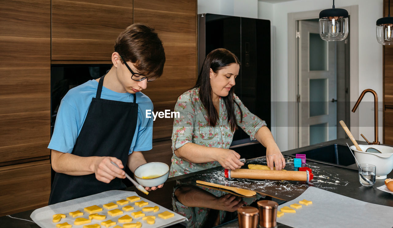 adult, kitchen, two people, women, indoors, food and drink, domestic kitchen, domestic room, food, home, togetherness, domestic life, female, person, lifestyles, standing, clothing, preparing food, cooking, cooperation, casual clothing, table, young adult, meal, bonding, kitchen counter, teamwork, waist up, home interior, looking down, men, apron, kitchen utensil, mature adult, looking, freshness, occupation, happiness, holding
