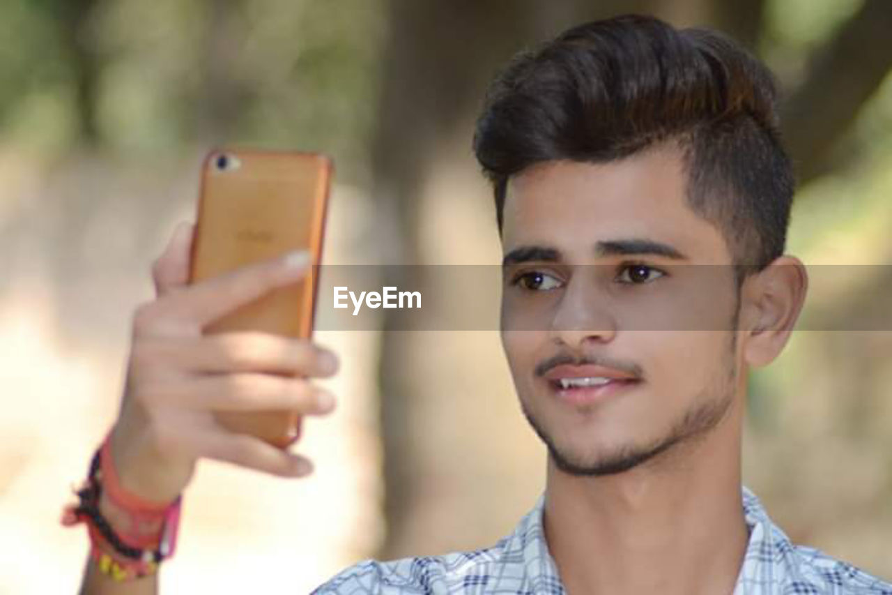 PORTRAIT OF SMILING YOUNG MAN USING SMART PHONE