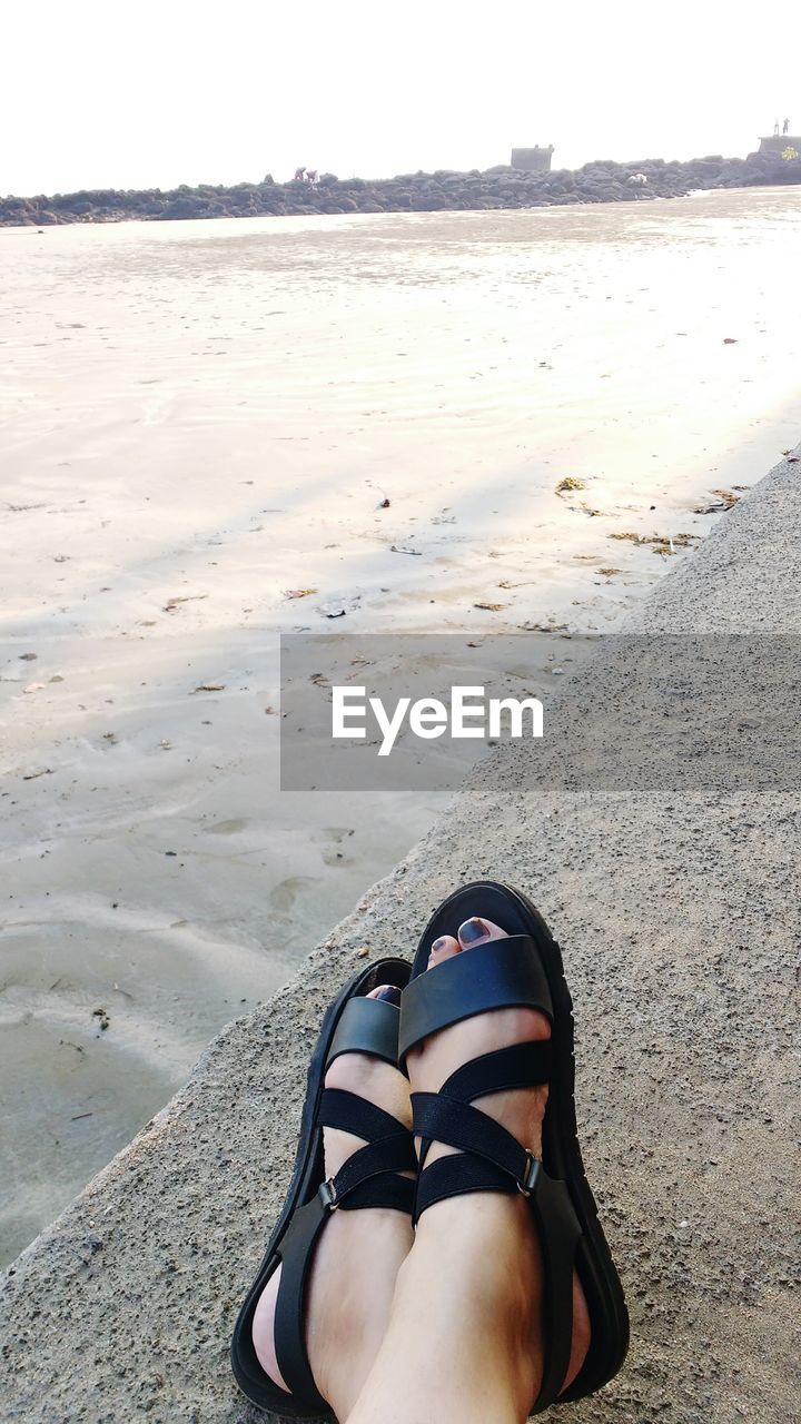 Low section of woman at beach against sky