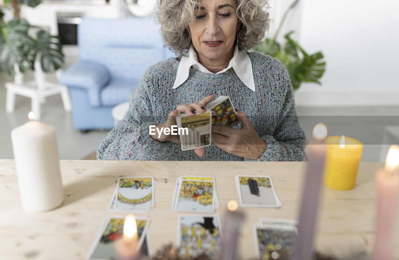 Senior woman reading tarot cards on table at home