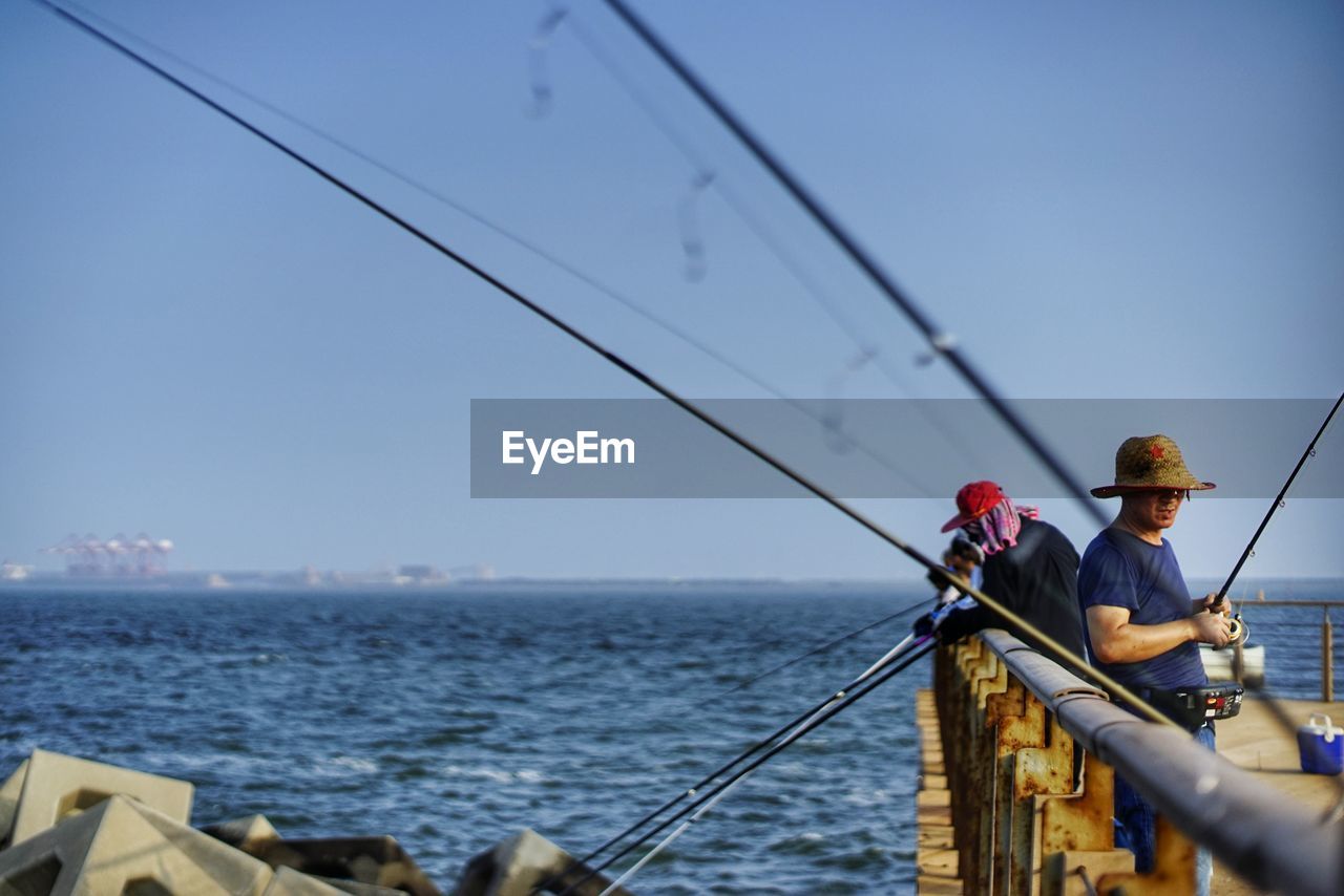 MAN FISHING ON BOAT AGAINST SKY