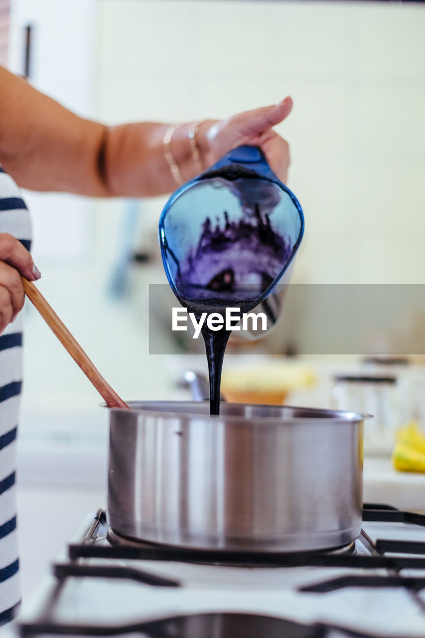 Midsection of woman preparing food in saucepan on stove in kitchen 