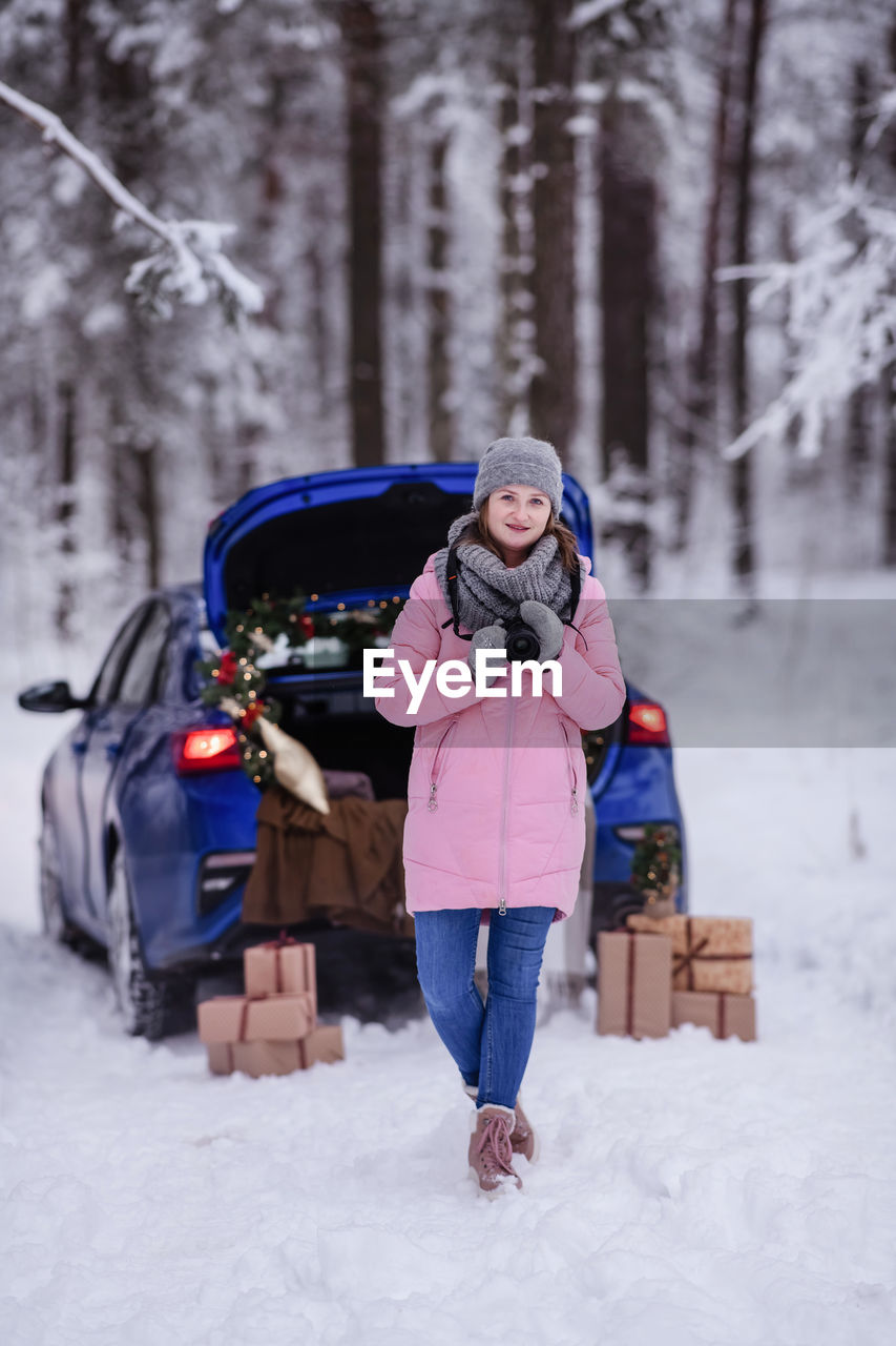 A woman in a winter snow-covered forest in the trunk of a car decorated with christmas decor.