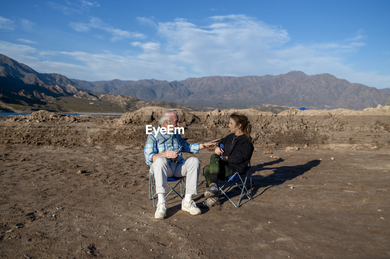 Woman and her grandfather talking while sitting on camping chairs outdoors in nature.