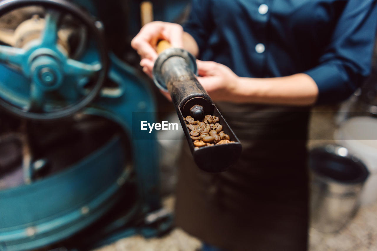 Midsection of worker showing coffee beans in sampling scoop