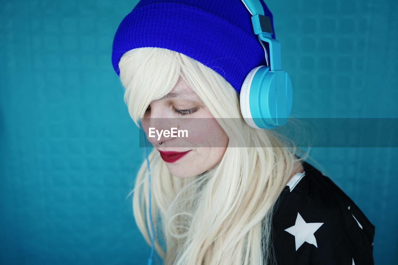 Close-up of woman with blond hair listening music against blue wall