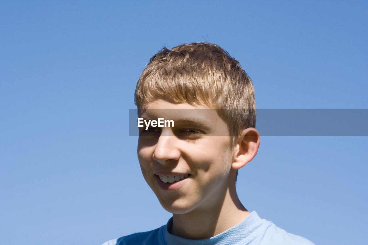 Low angle view of smiling man against clear blue sky