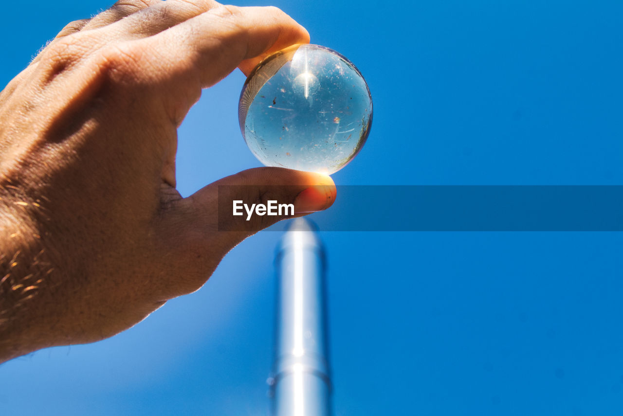 Close-up of hand holding crystal against blue sky