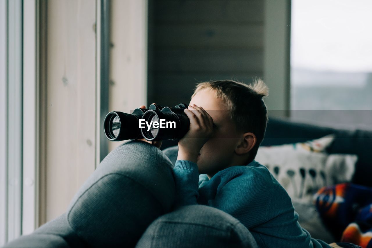 Young boy looking through binoculars at nature from a cosy cabin