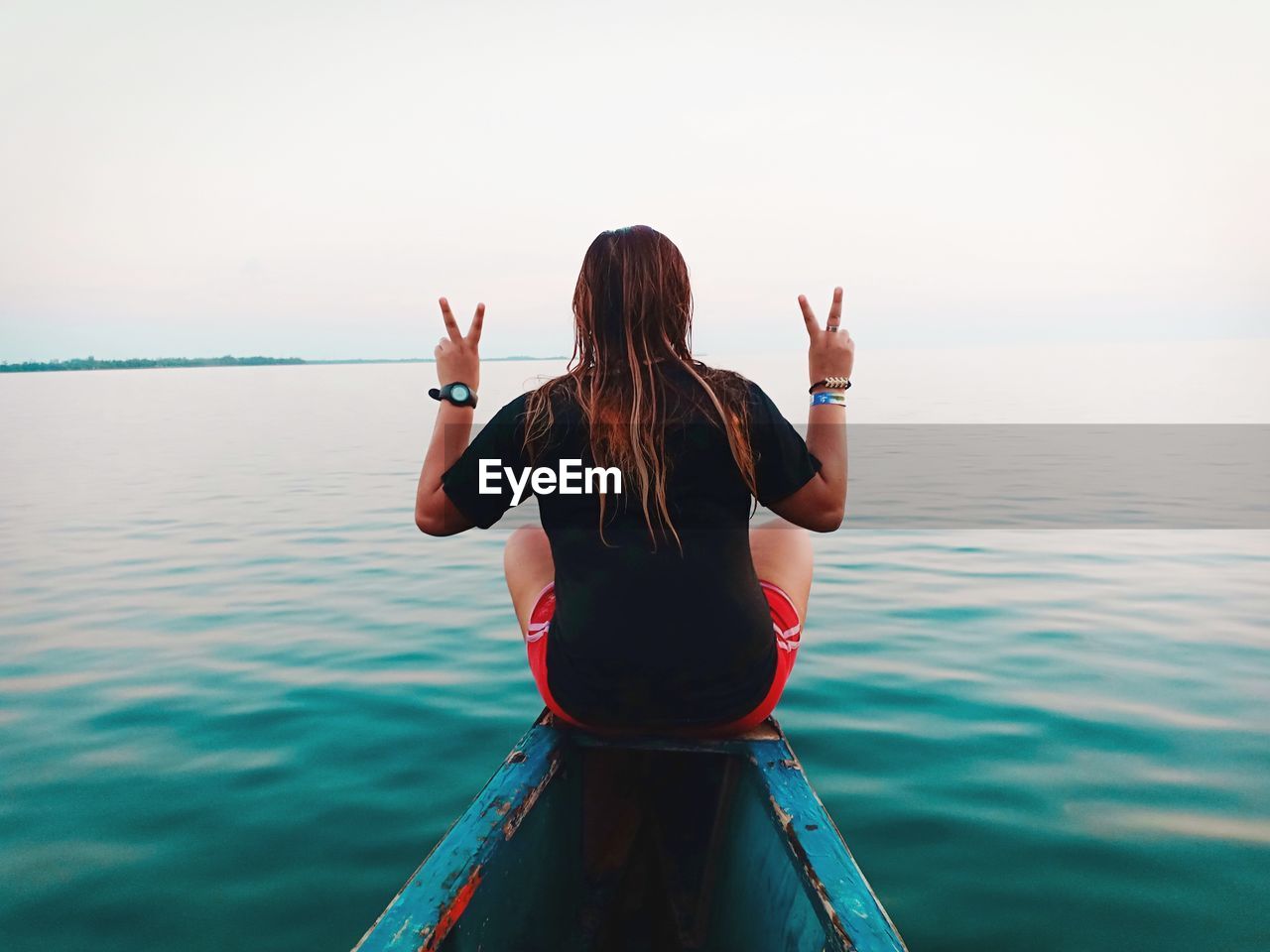 Rear view of woman showing peace sign on boat in sea against sky