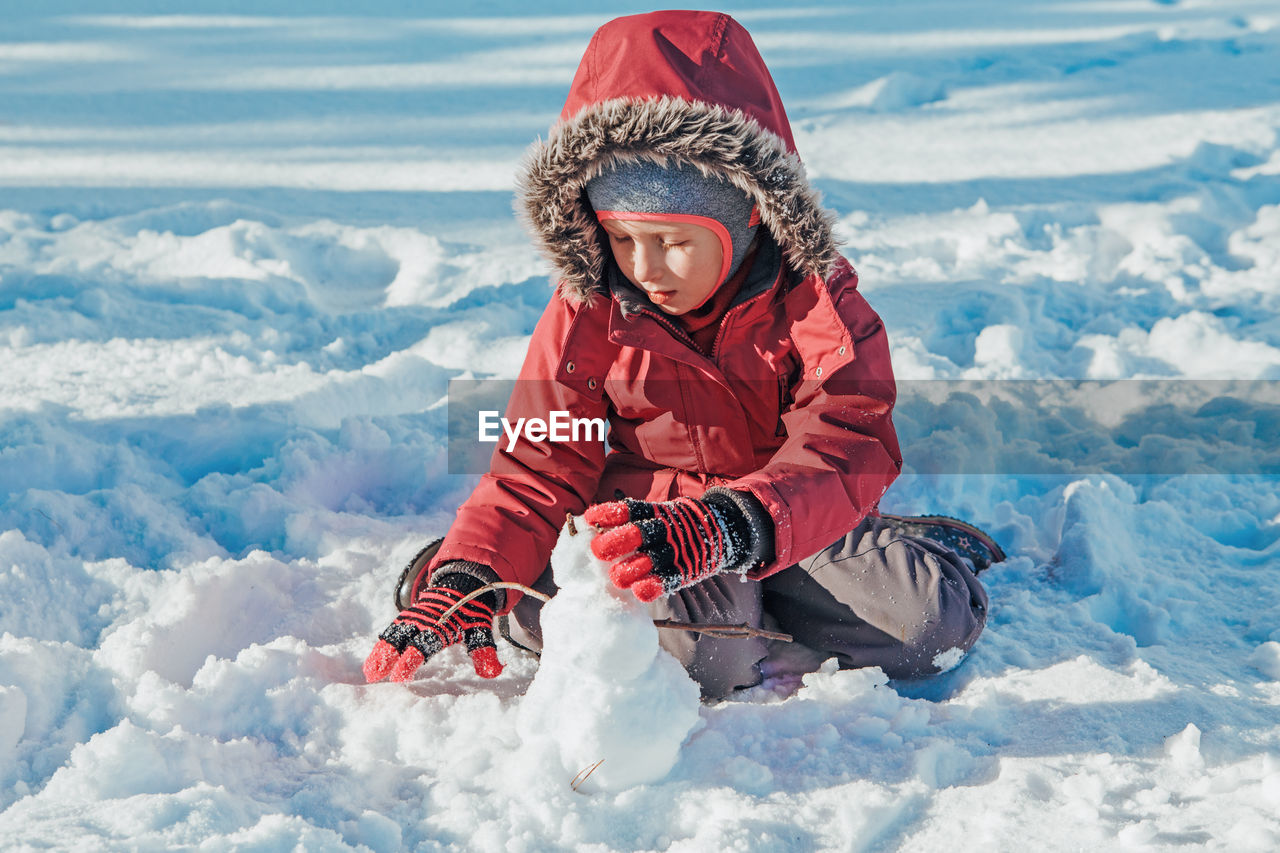 Girl child in warm clothes playing with snow in park outside. kids outdoor seasonal activity.