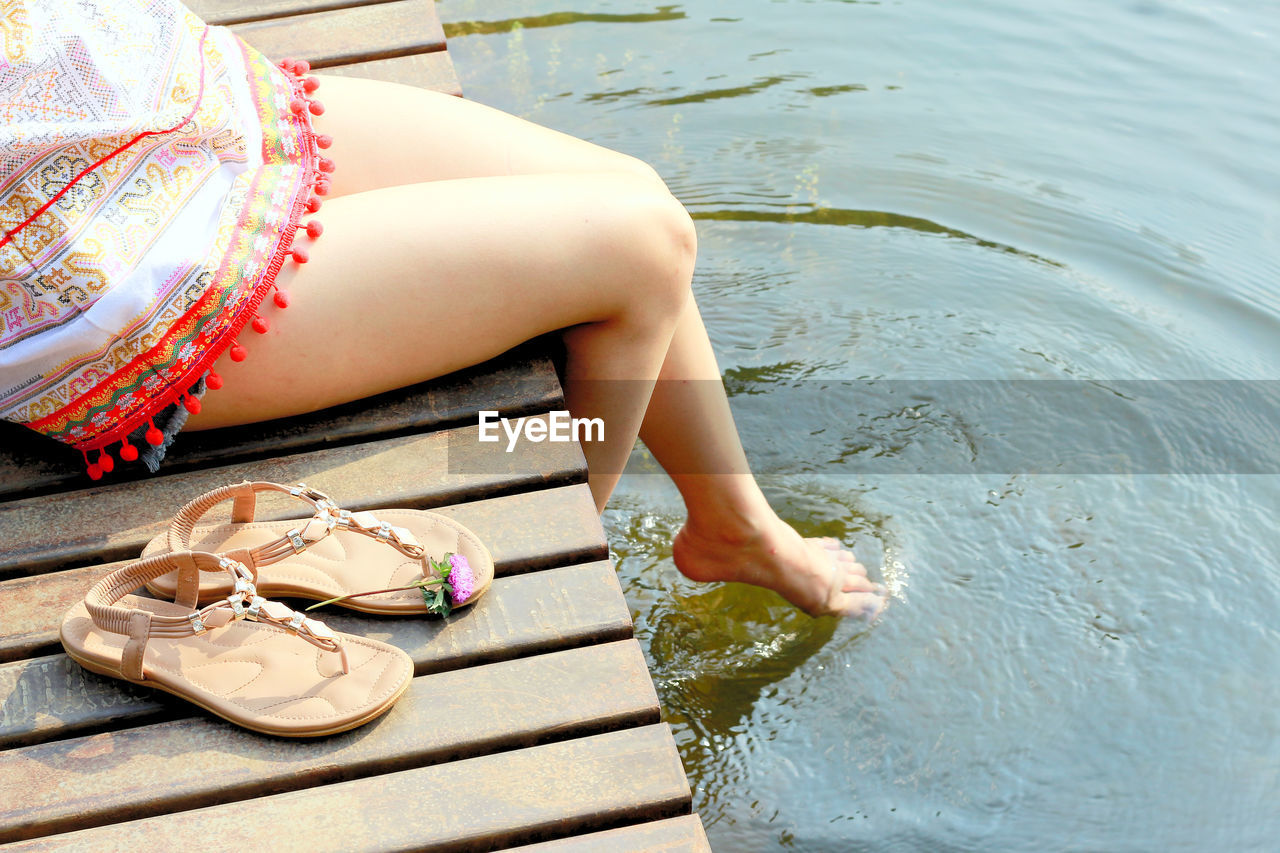 Low section of woman sitting on pier over lake