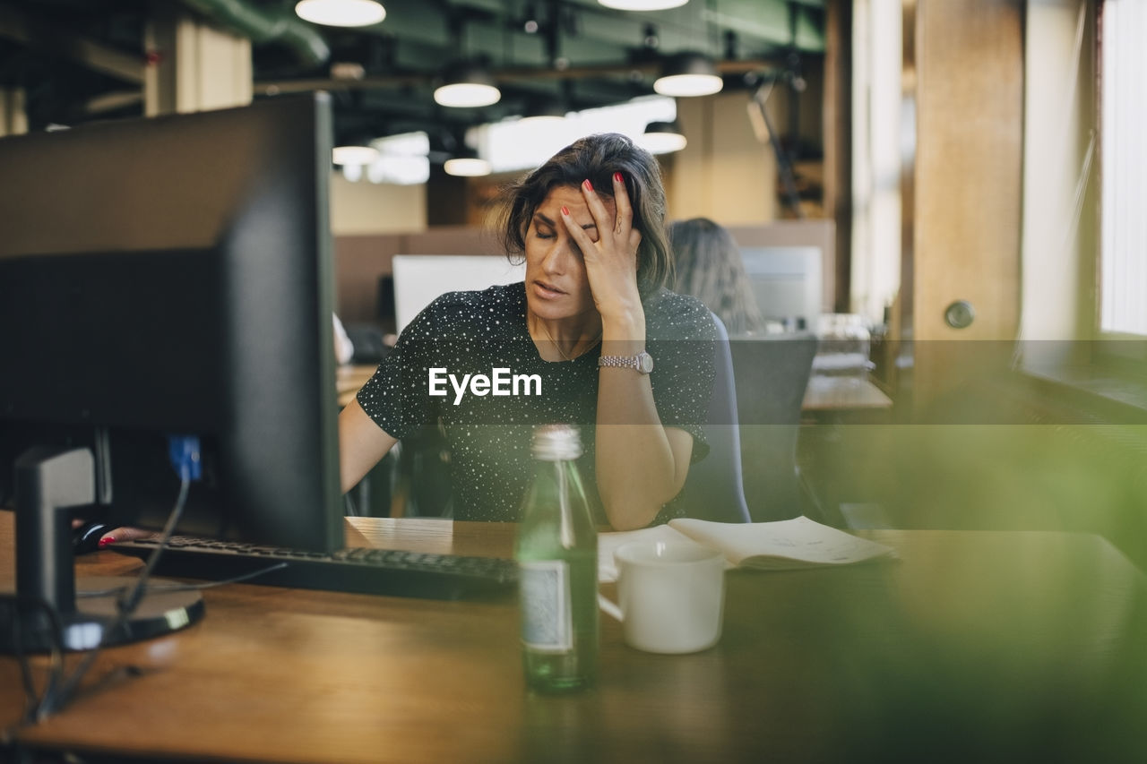 Tired businesswoman with head in hand sitting at computer desk in office