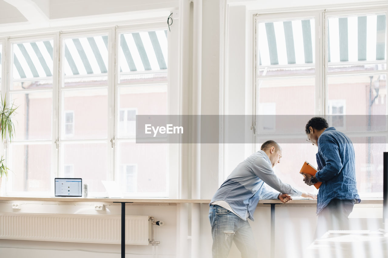 Male computer programmers discussing at desk by window in office