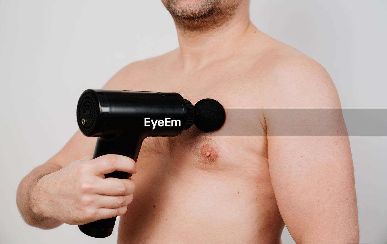 Midsection of shirtless man using percussion massager