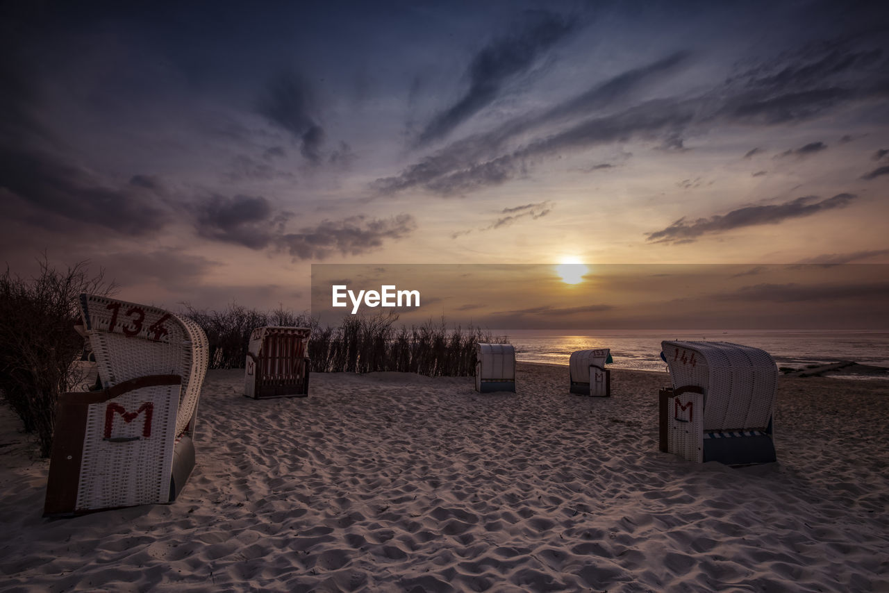 Hooded beach chairs on sand against sky during sunset