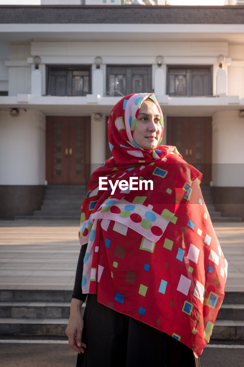 Woman wearing red scarf while standing against building in city