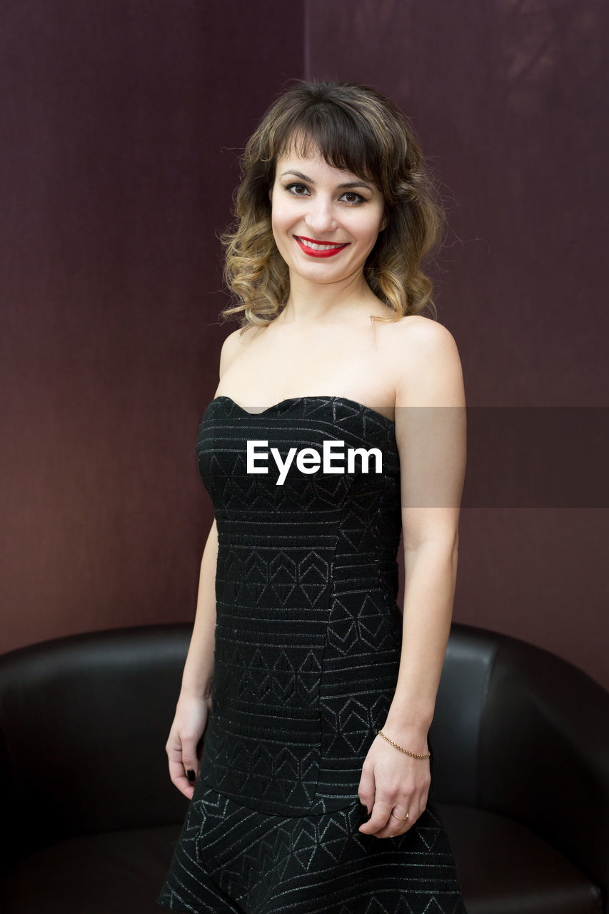 Portrait of woman smiling while standing against wall