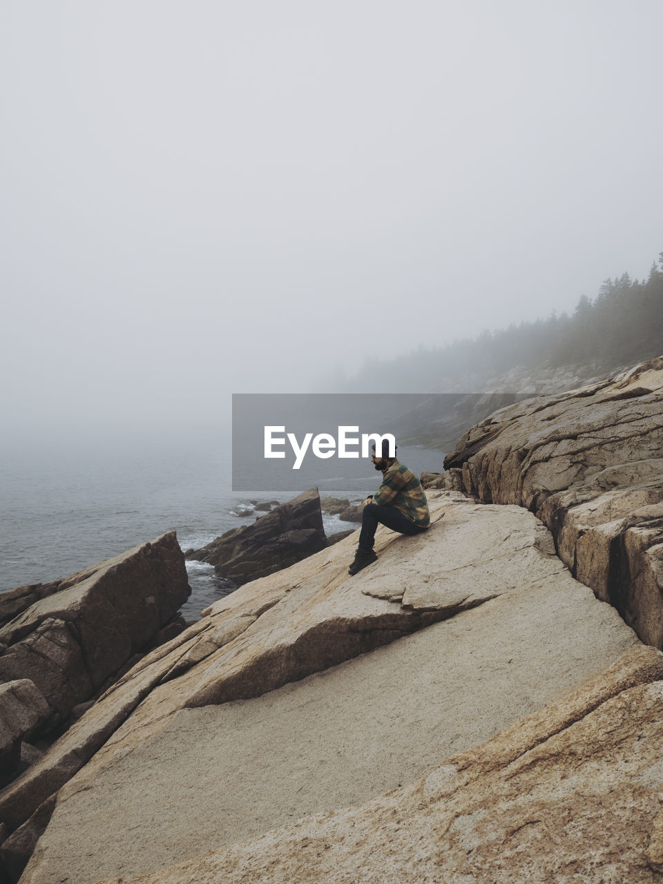 Full length of man sitting on rock by sea against clear sky