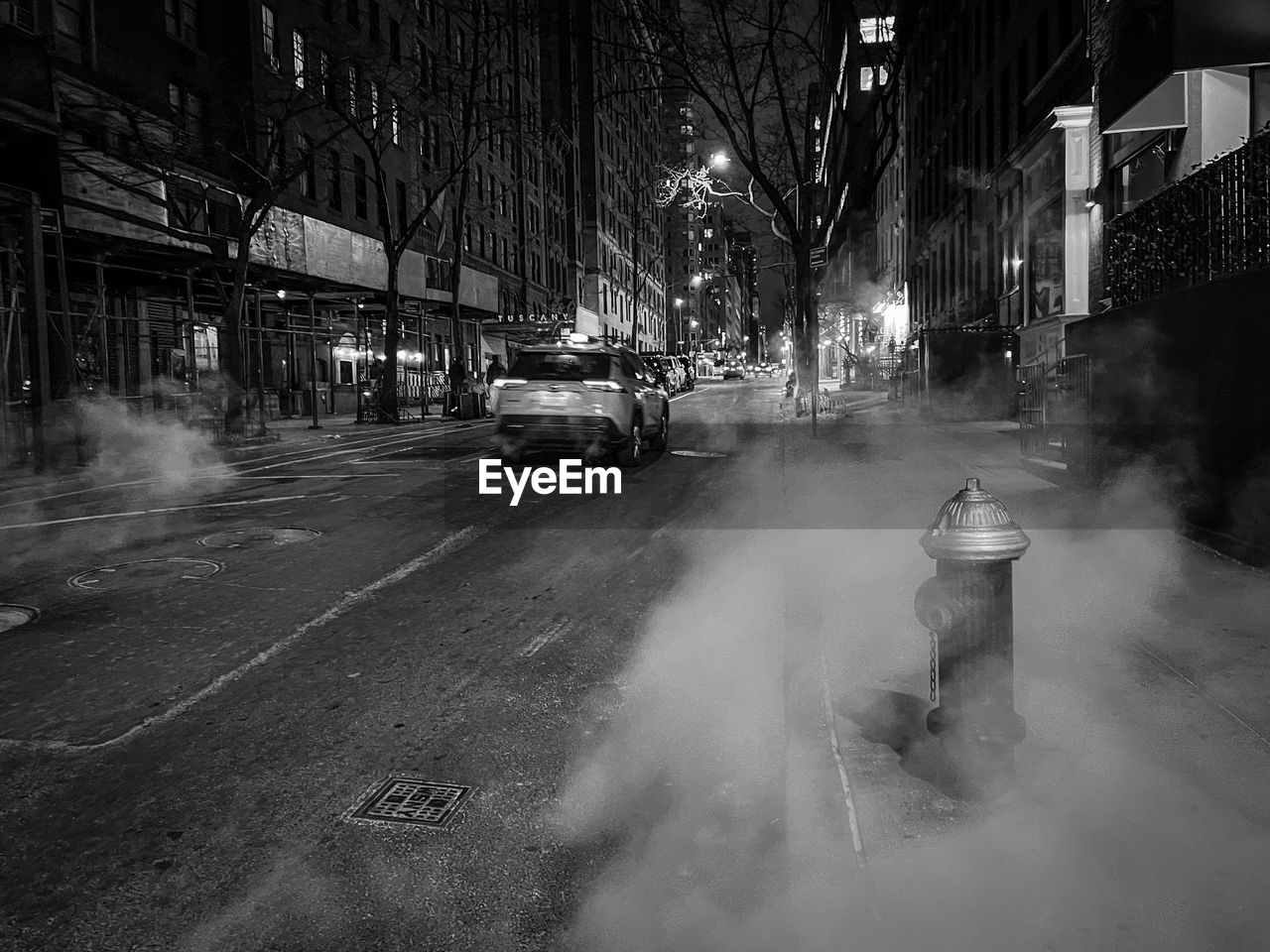 darkness, transportation, mode of transportation, city, street, car, road, architecture, motor vehicle, building exterior, land vehicle, snow, fog, night, monochrome, black and white, smoke, built structure, black, city street, monochrome photography, motion, sign, winter, infrastructure, illuminated, vehicle, light, city life, nature, outdoors, tree