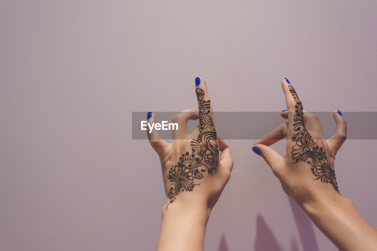 Cropped hands of woman with henna tattoo against purple background