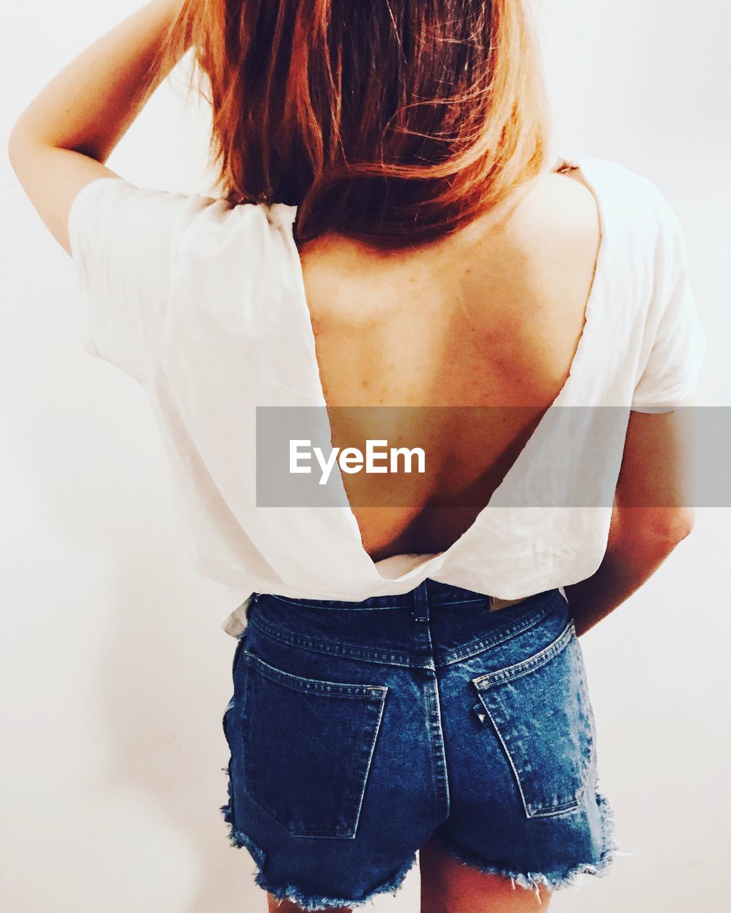 Rear view of young woman backless top against white wall