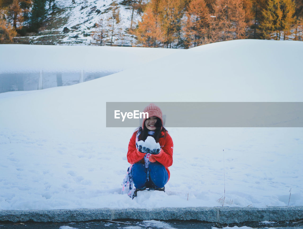 Cheerful woman with snow crouching at forest