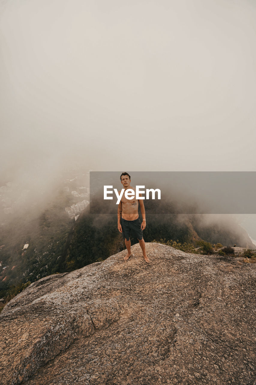 Young man standing on rock against sky