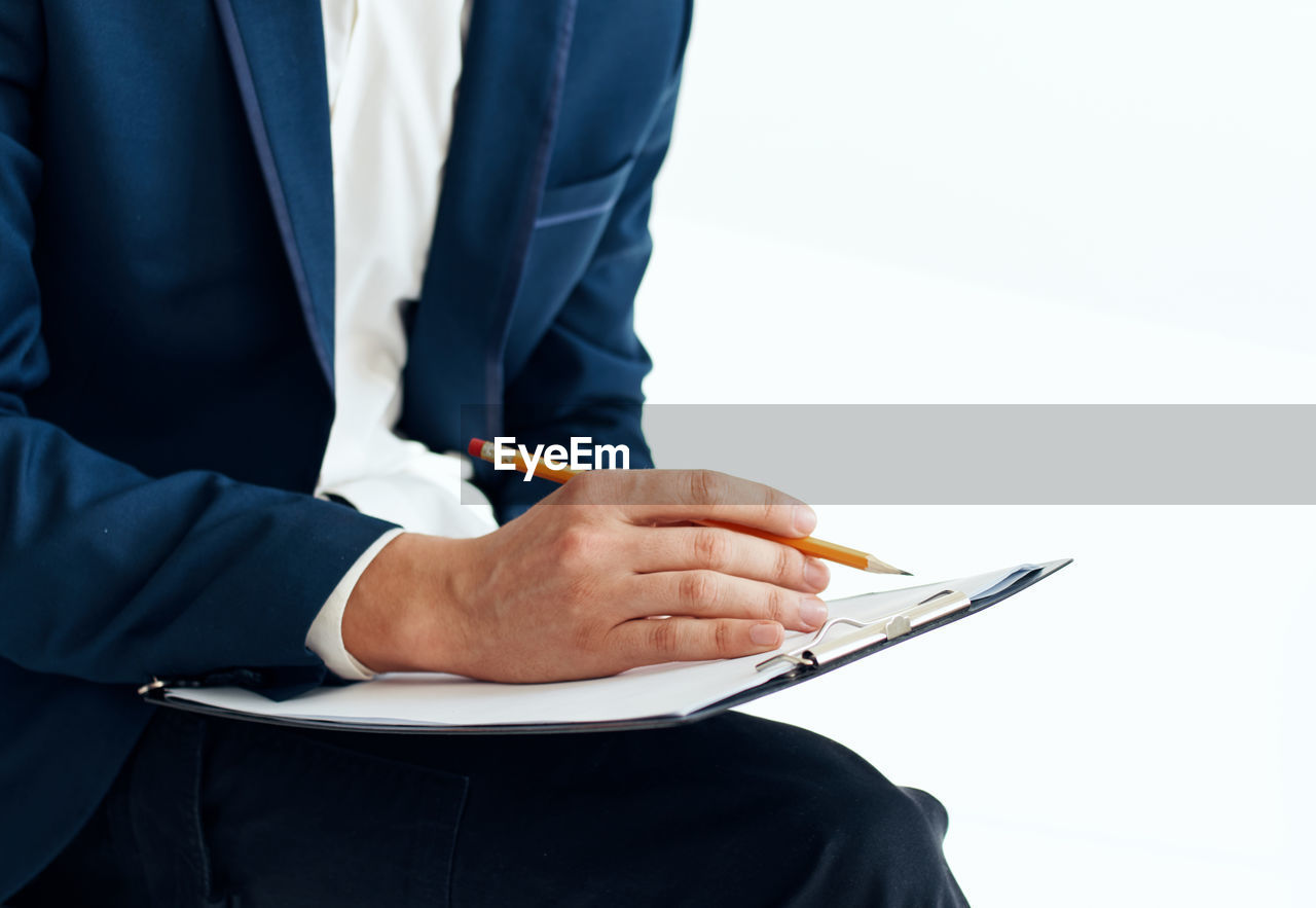 Midsection of businessman holding pencil and clipboard against white background