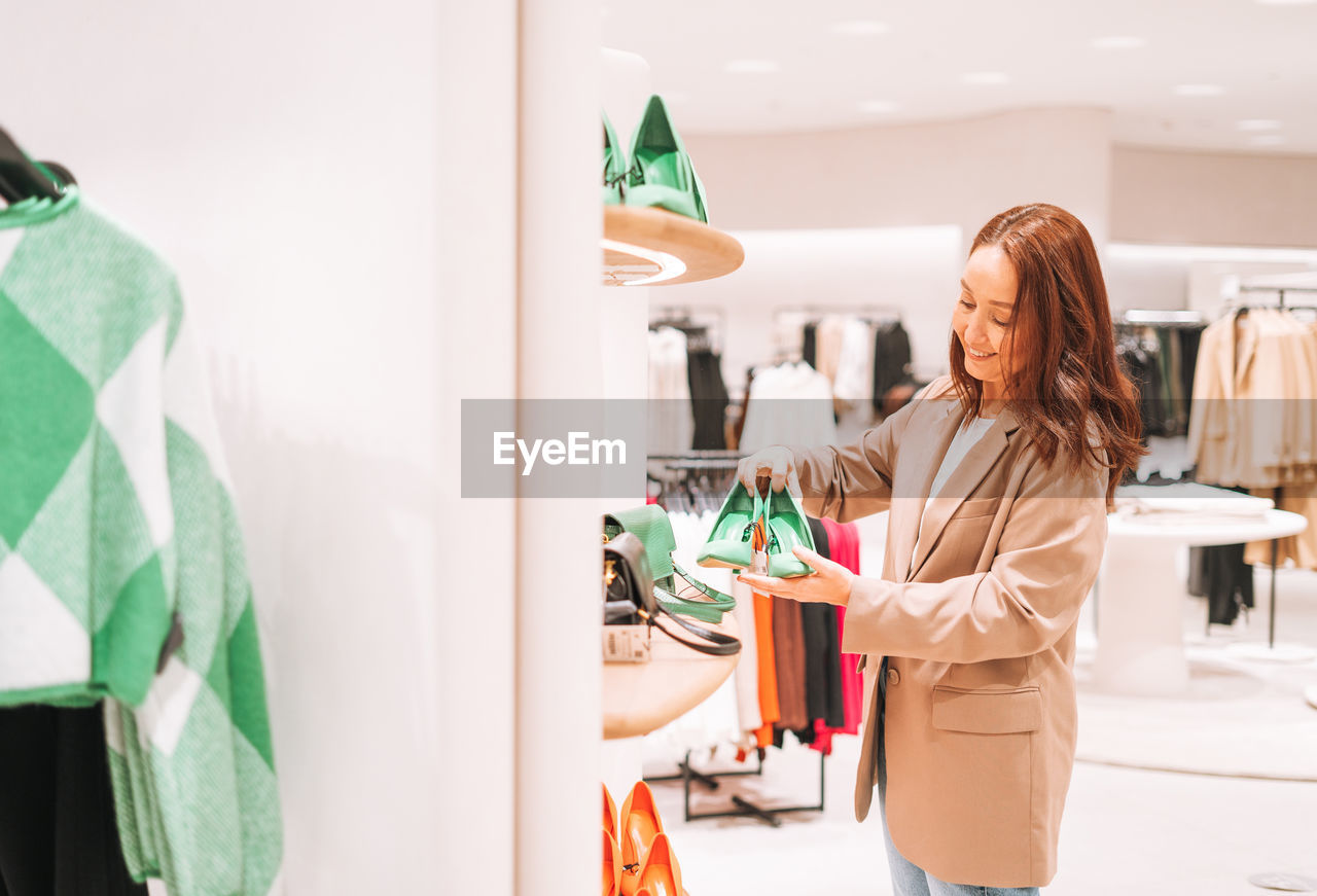 Adult brunette woman in beige suit and jeans chooses shoes at shopping mall