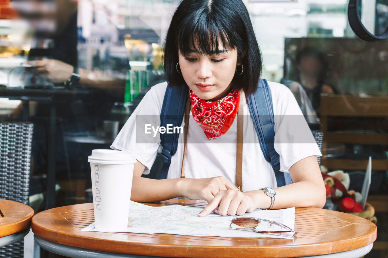 Young woman reading map while sitting at sidewalk cafe