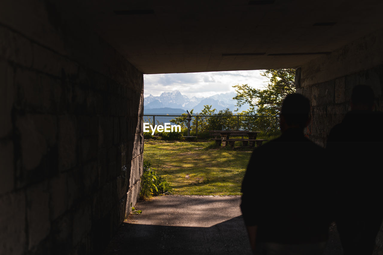 Rear view of silhouette man standing by wall against sky