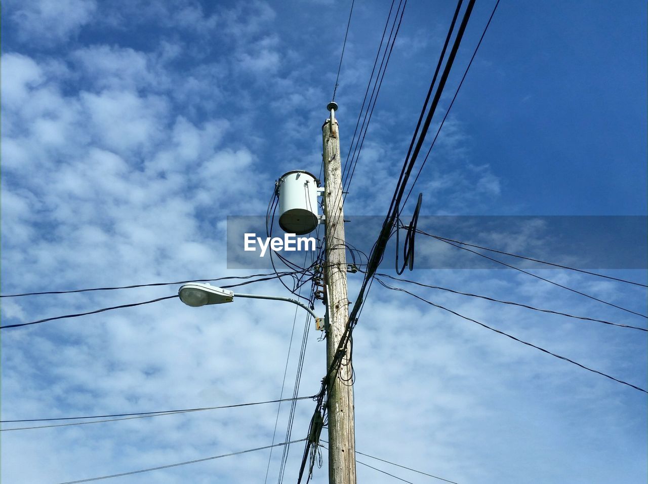 Low angle view of electricity pole against cloudy sky