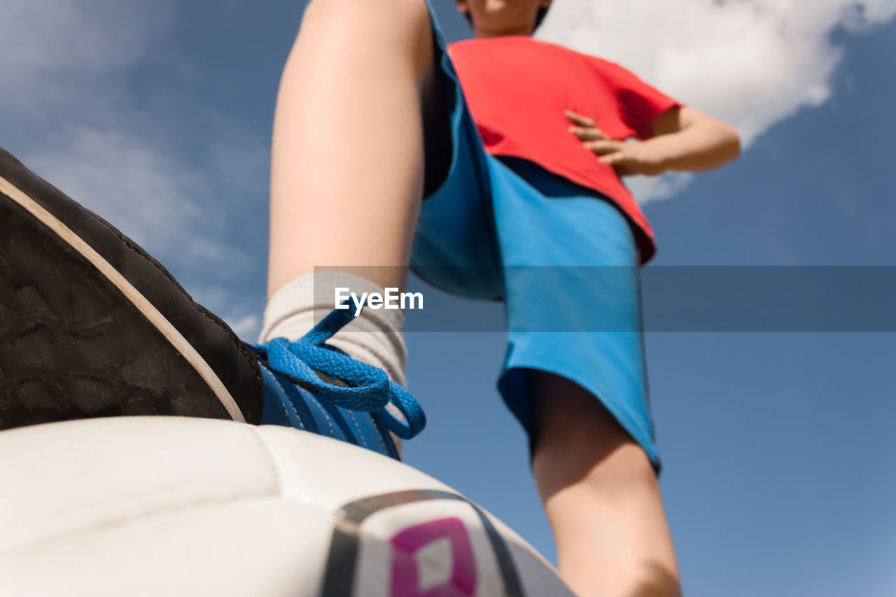 Low section of boy standing on ball against blue sky