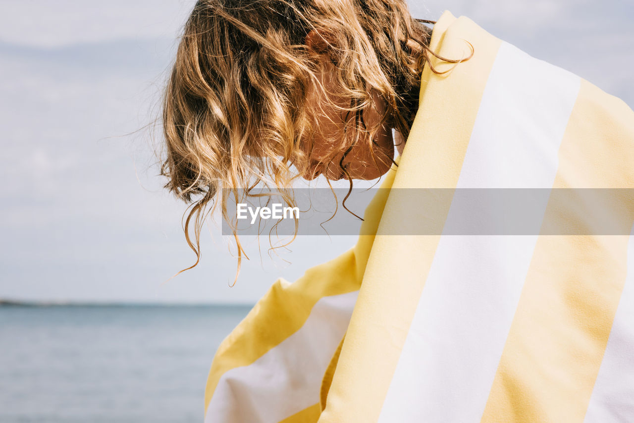 Young girl with curly hair wrapped in a striped towel at the beach