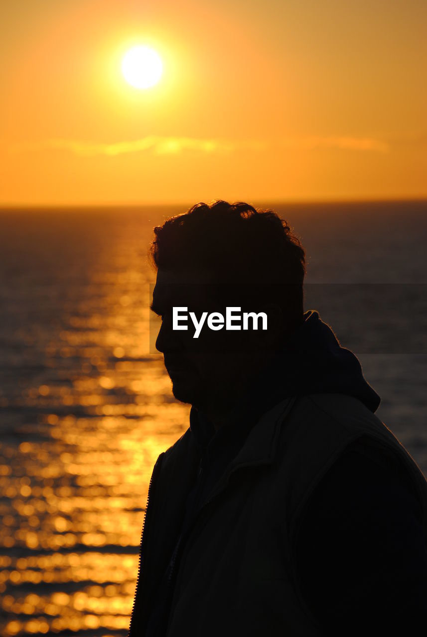 SILHOUETTE MAN ON ROCK AGAINST SEA DURING SUNSET