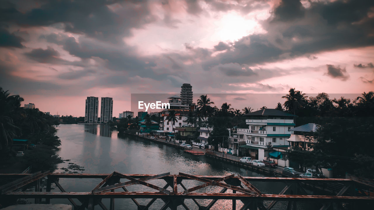 River by buildings against sky at sunset