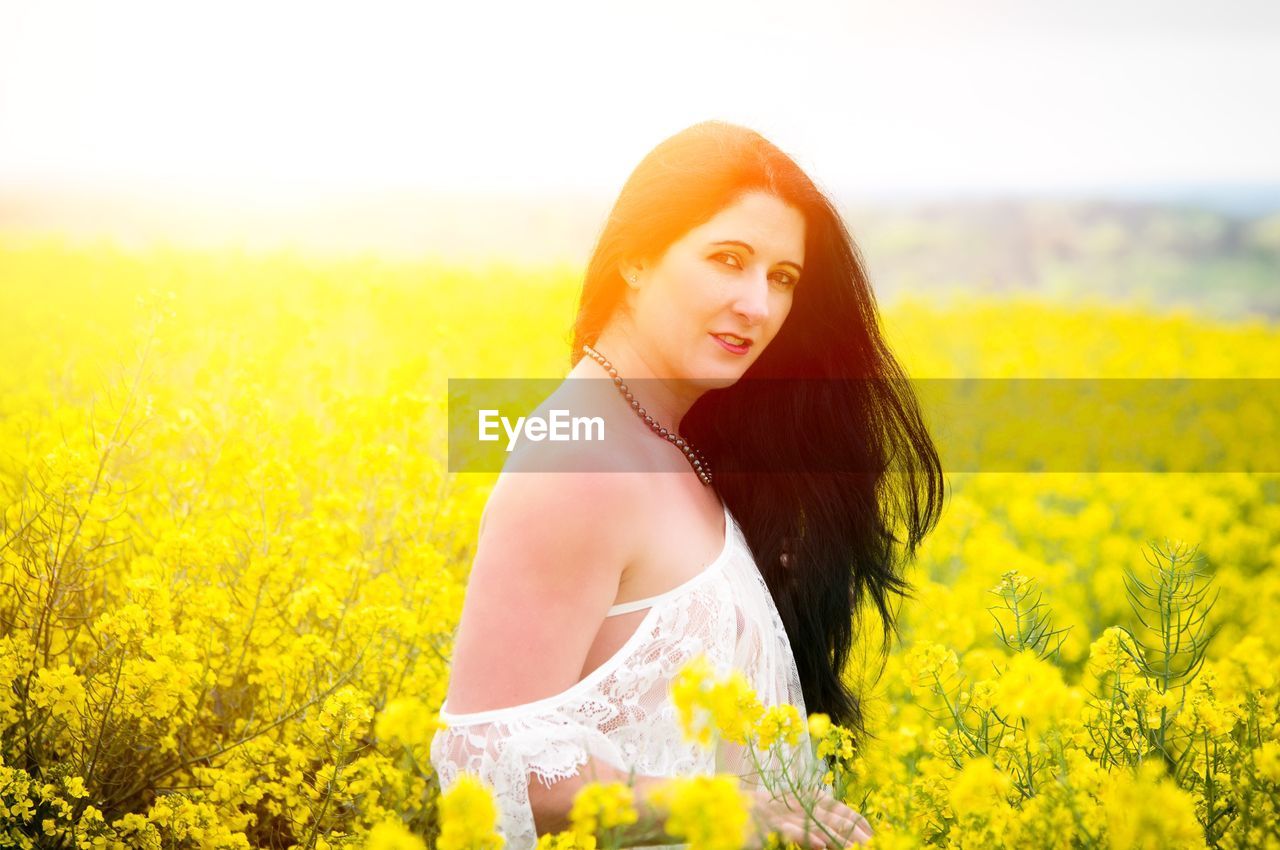 PORTRAIT OF BEAUTIFUL WOMAN STANDING ON FIELD WITH YELLOW FLOWERS