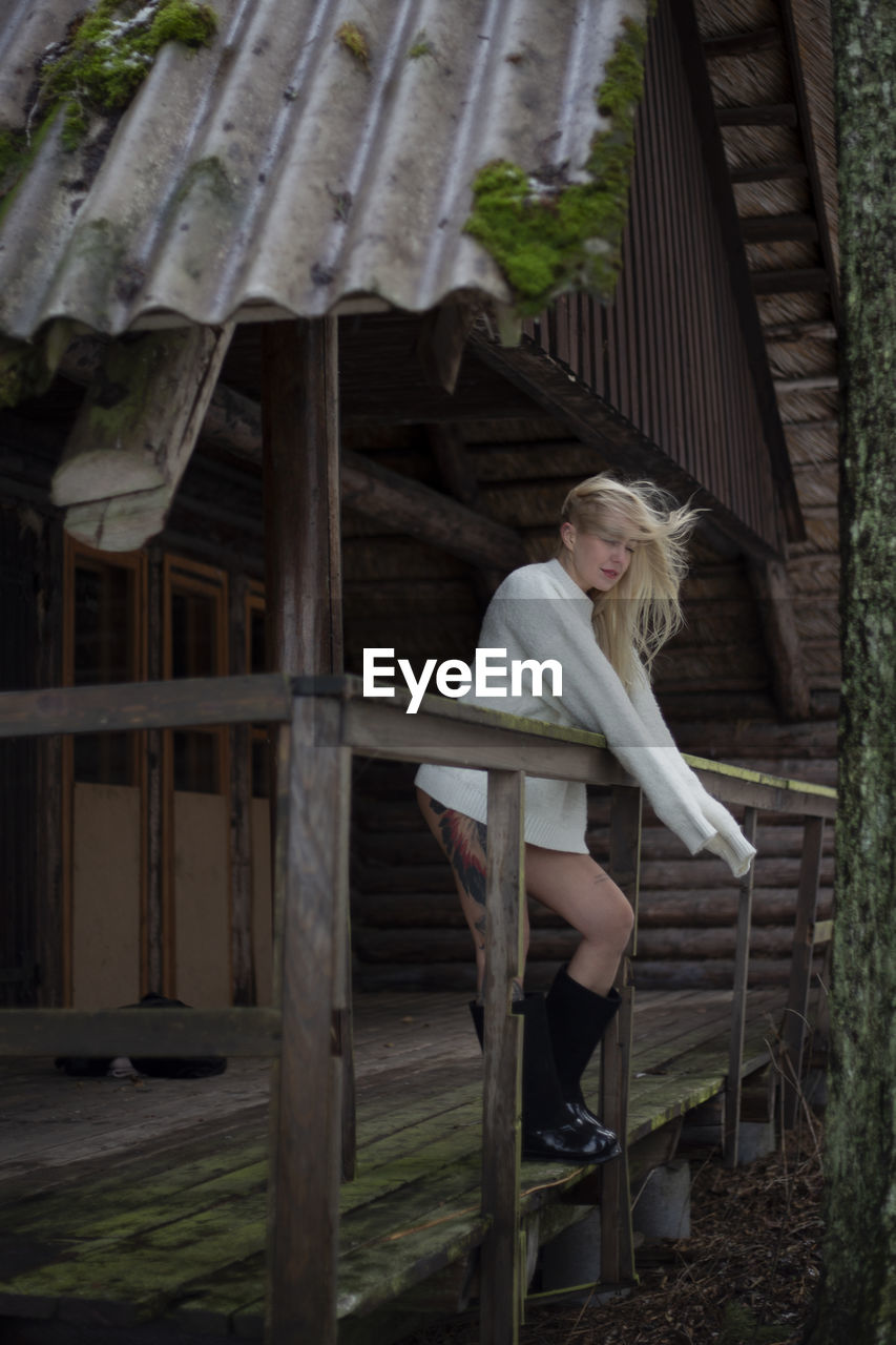 Portrait of young woman sitting on wooden wall