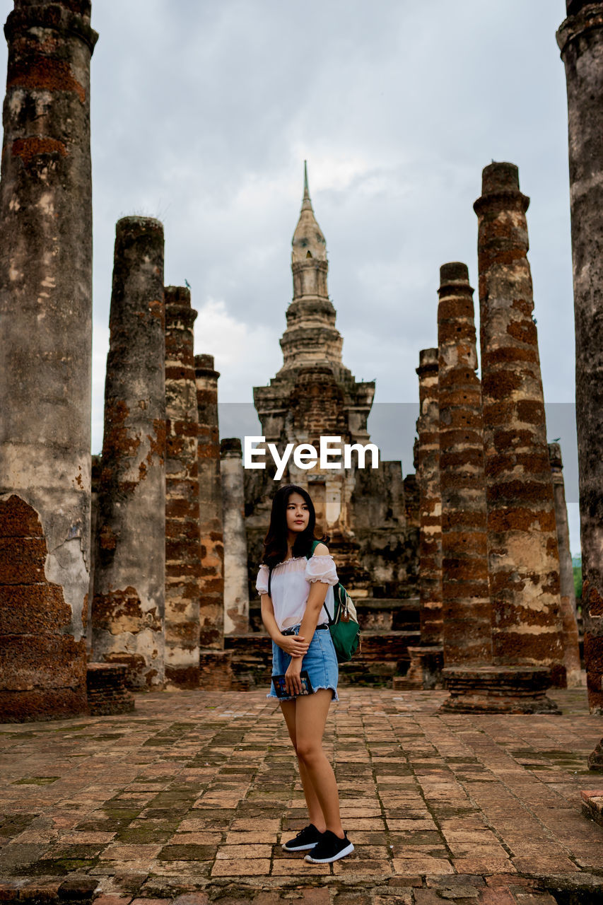 FULL LENGTH OF YOUNG WOMAN STANDING AGAINST TEMPLE BUILDING