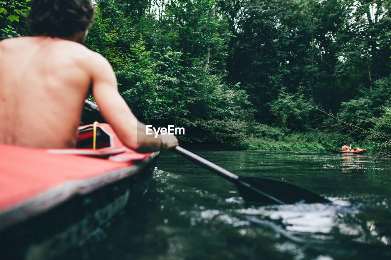Shirtless man kayaking in lake at forest