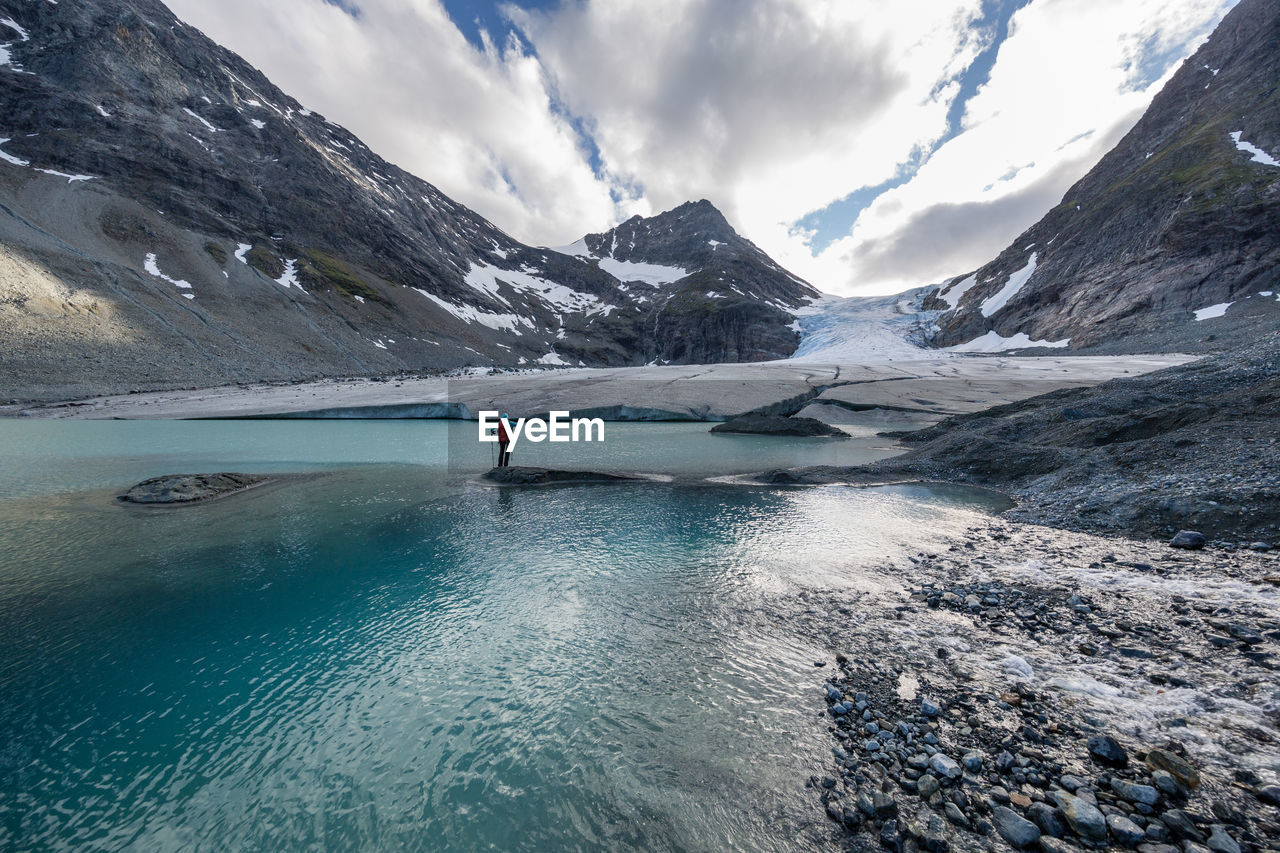 Rear view of hiker standing on rocks amidst river