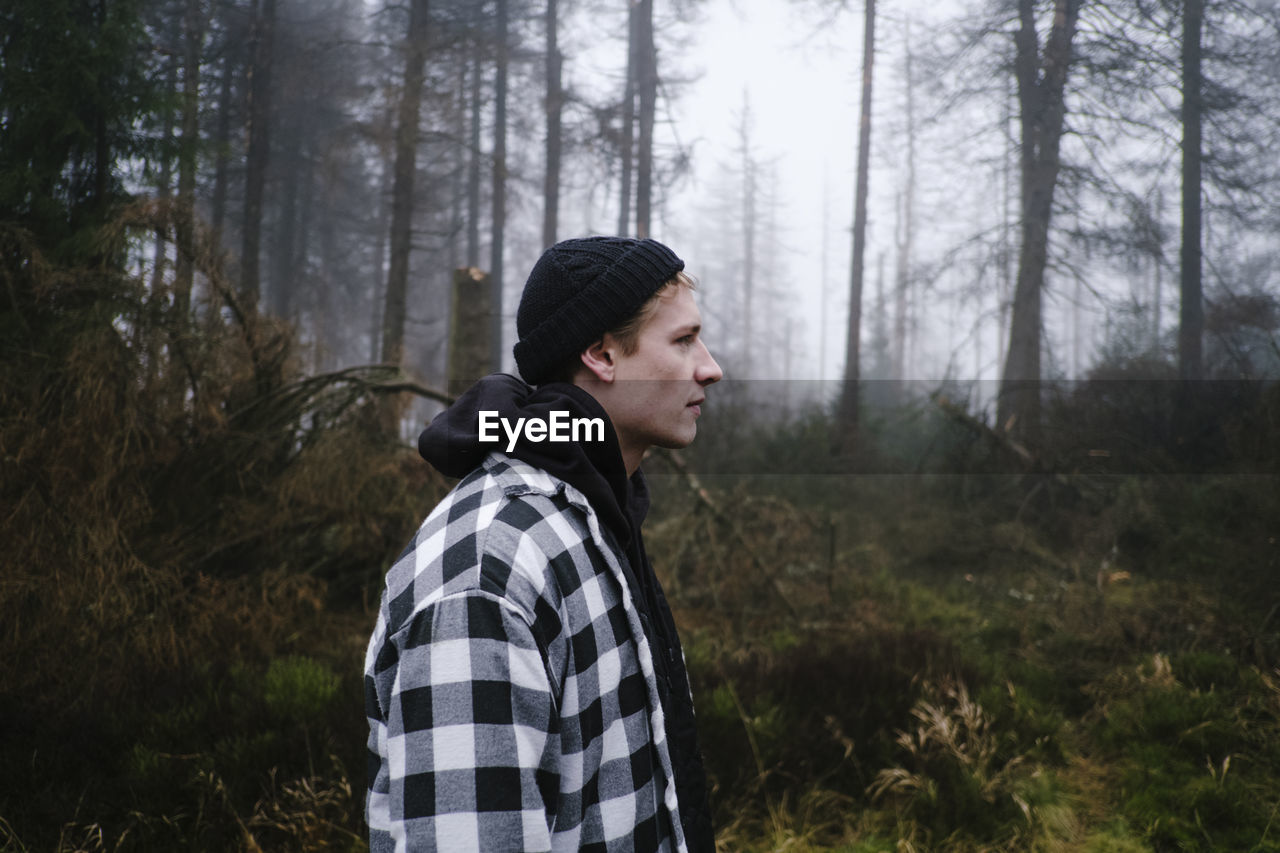 Side view of man looking way while standing in forest