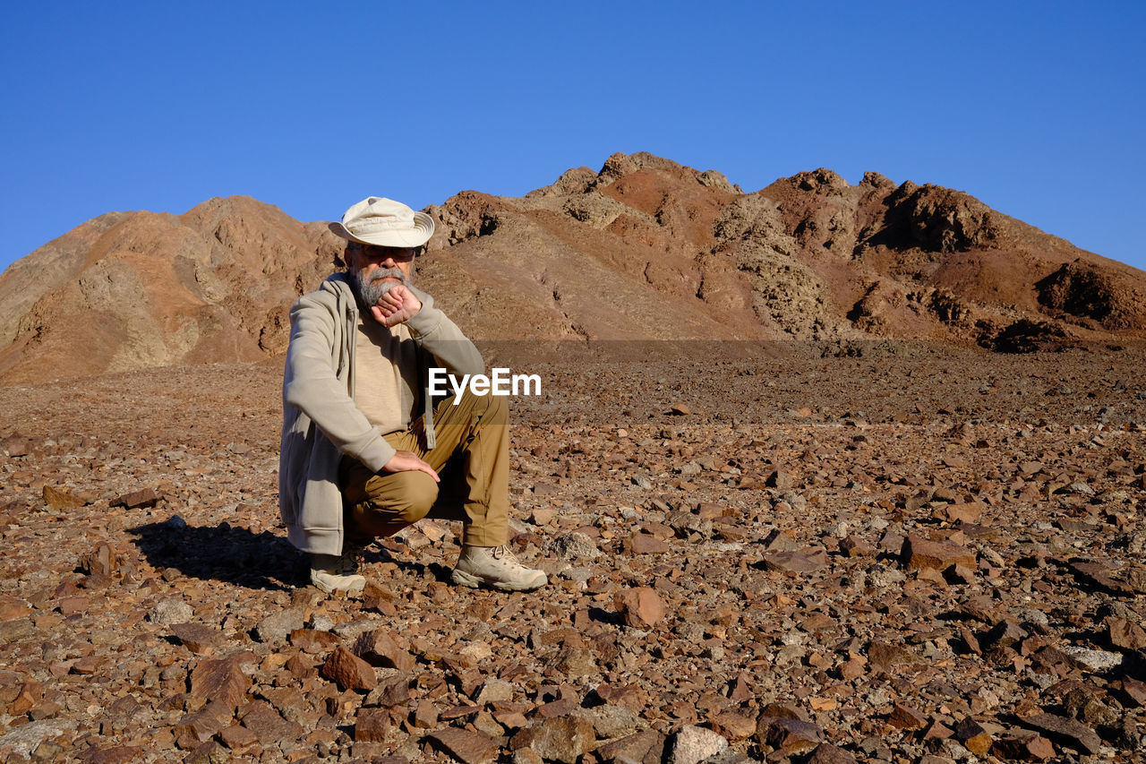 Senior man sitting on rock against clear sky at desert 