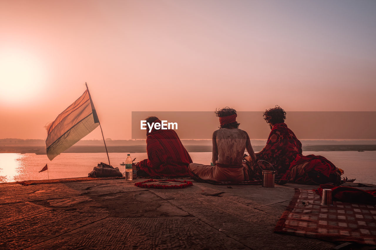 People sitting by sea against sky during sunset