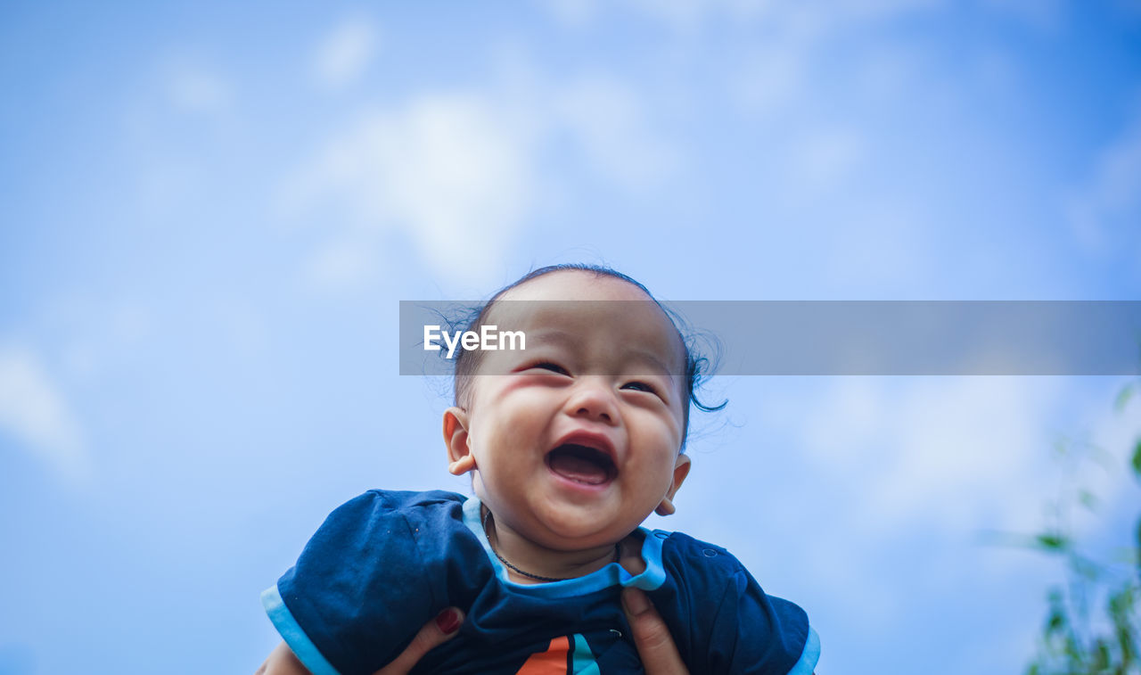 Cropped image of mother picking up baby against sky