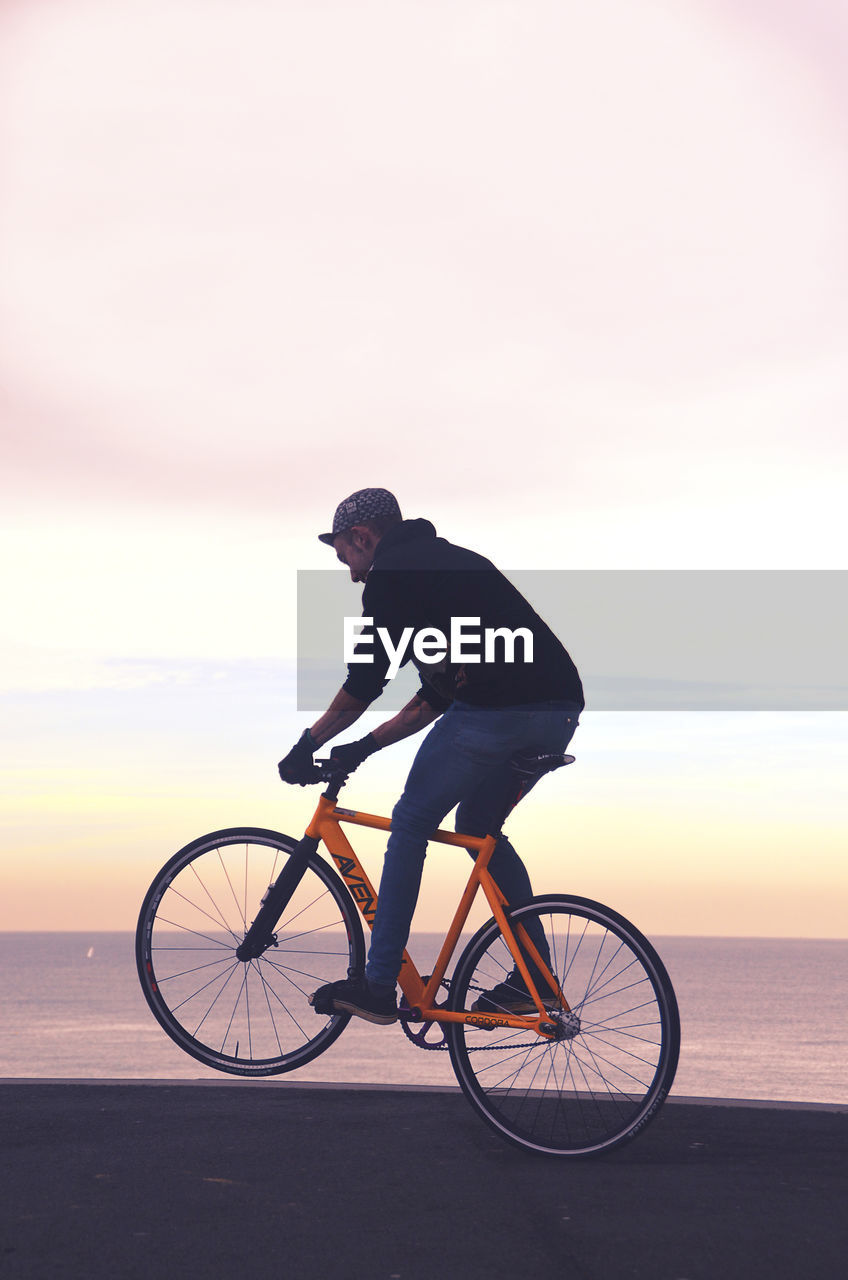 SIDE VIEW OF MAN RIDING BICYCLE ON SHORE