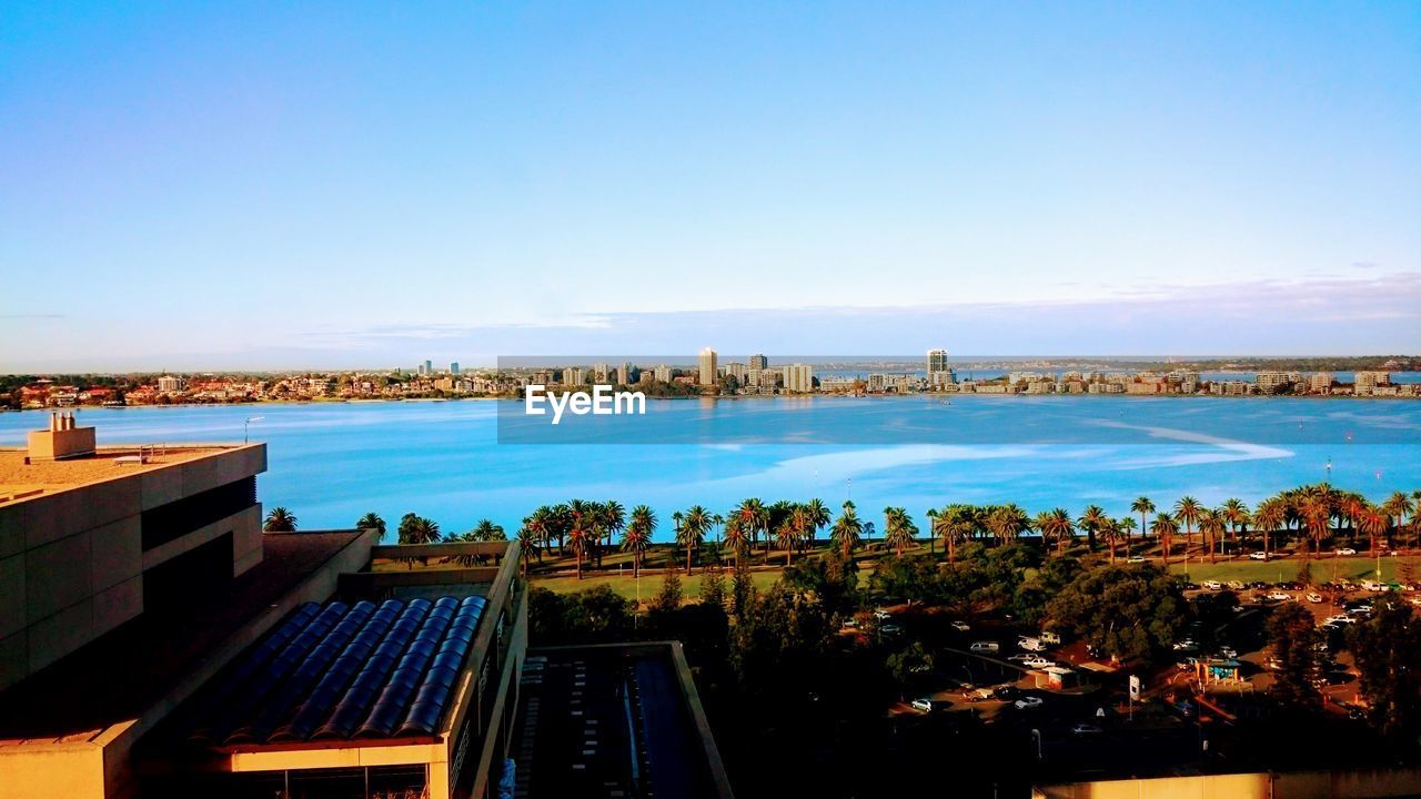 HIGH ANGLE VIEW OF SWIMMING POOL BY BUILDINGS AGAINST CLEAR BLUE SKY