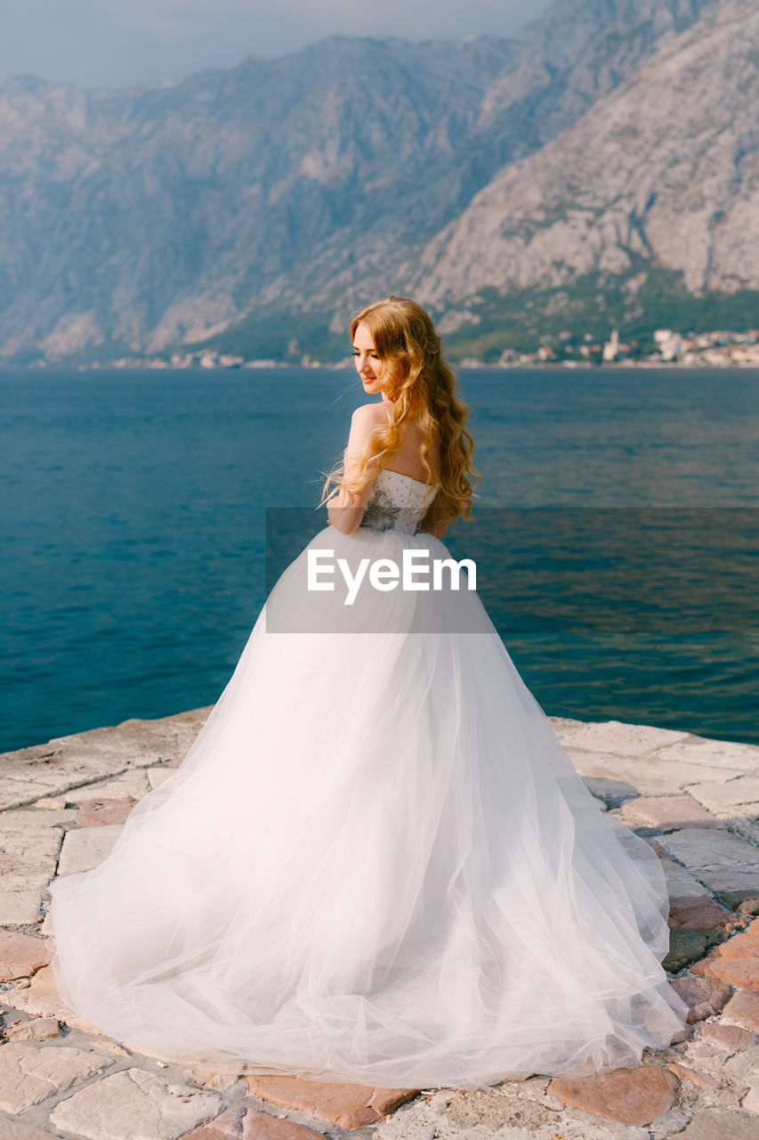 Woman standing on rock by sea against mountain