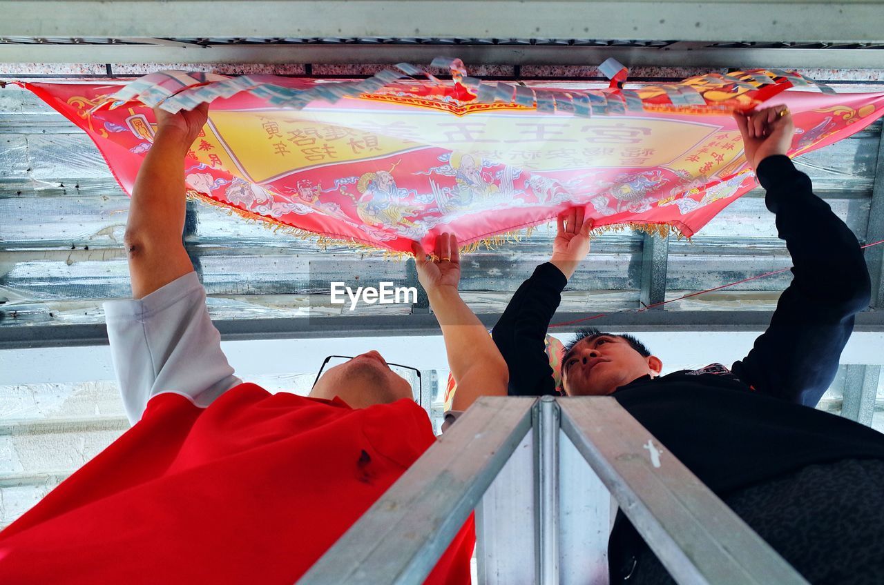 Men adjusting red textile on ceiling